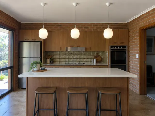 Three white pendant lights above a kitchen island in a brick and timber kitchen in San Remo